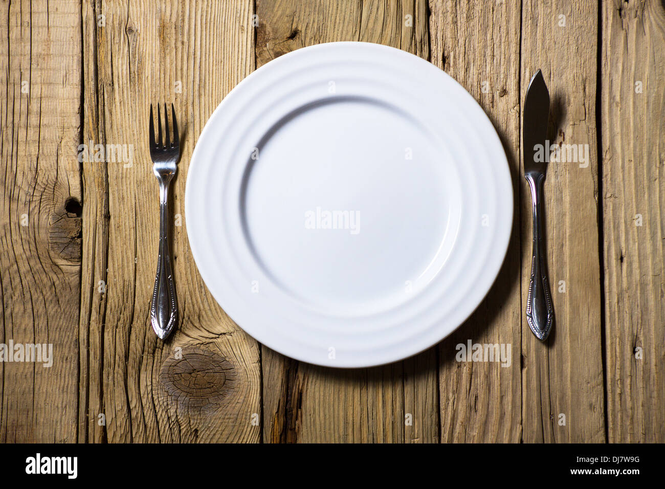 Posate e piastra bianca su tavola in legno rustico Foto Stock
