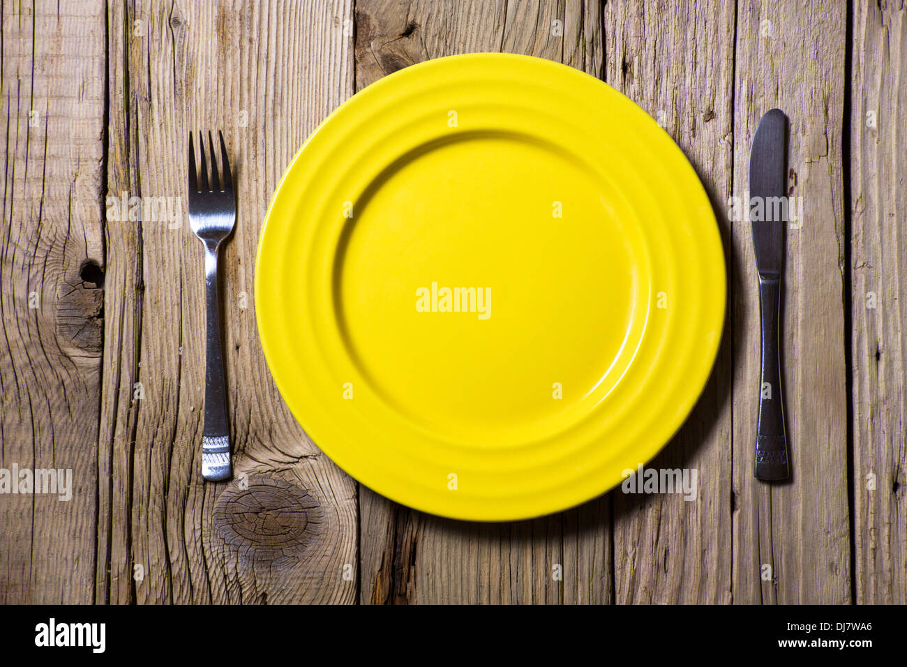 Posate e piastra di colore giallo su tavola in legno rustico Foto Stock