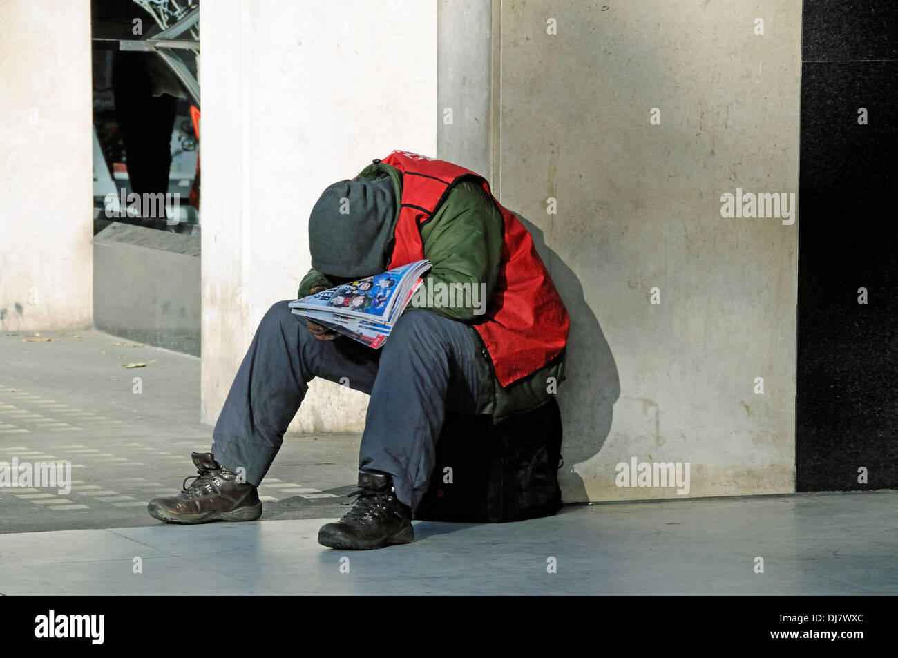 Grande problema venditore avvolto caldamente contro il freddo e addormentato in inverno il sole, Central London, England Regno Unito Foto Stock