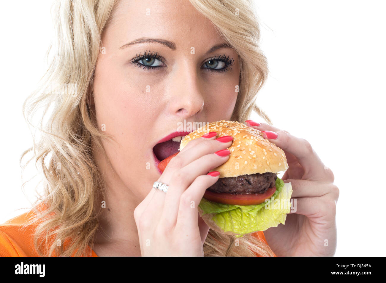 Fiducioso positivo felice giovane donna di mangiare un hamburger di manzo in una pagnotta di pane con pomodori e lattuga guarnire isolata contro uno sfondo bianco Foto Stock
