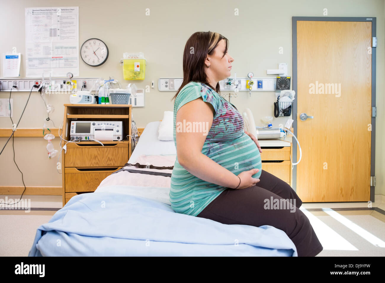 Donna incinta con le mani sul ventre sul letto di ospedale Foto Stock
