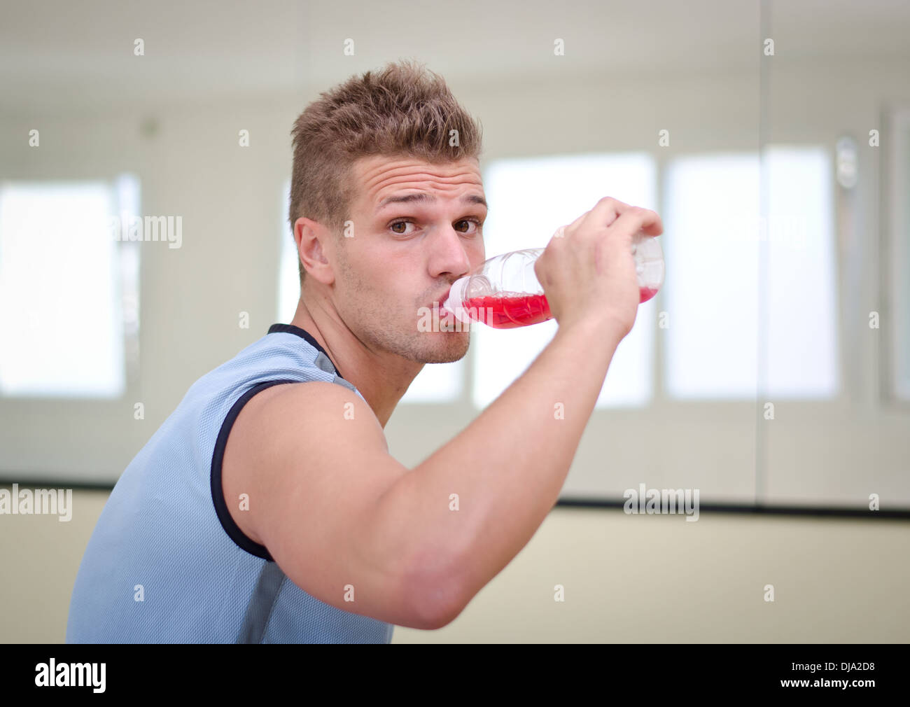 Attraente, bella atleta maschio rosso da bere una bevanda dalla bottiglia di plastica. Foto Stock