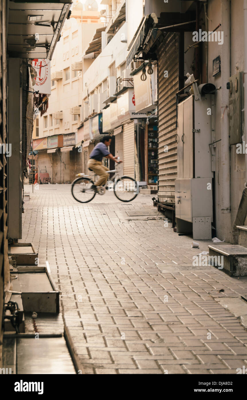 Un uomo in bicicletta attraverso le strette strade di Deira. Dubai, Emirati Arabi Uniti. Foto Stock