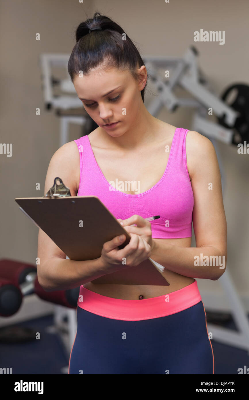 Grave allenatore femmina con blocco per appunti in palestra Foto Stock
