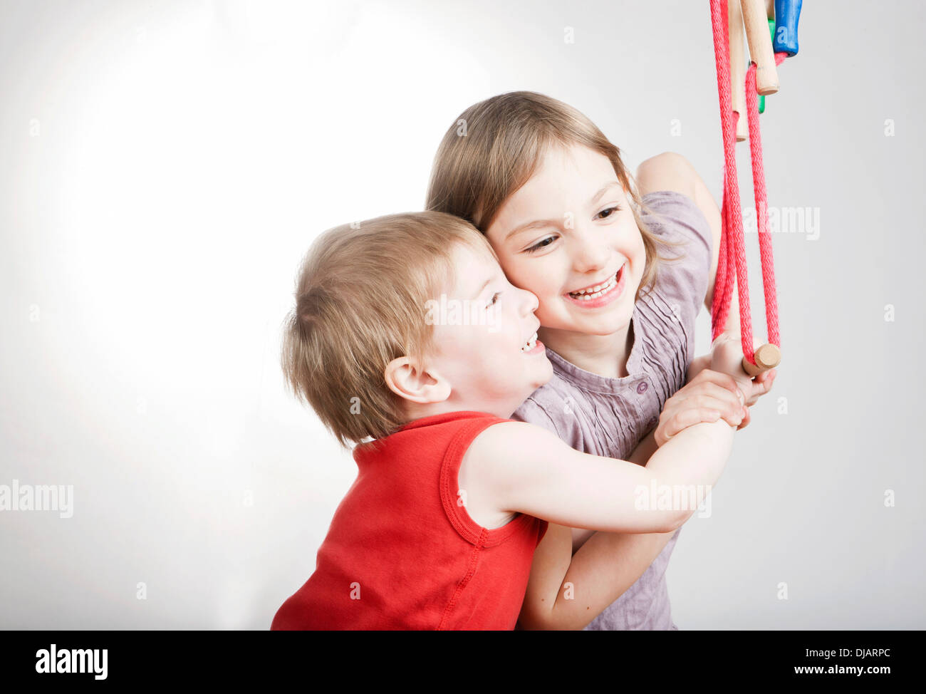 Un ragazzo e una ragazza, fratelli, tenendo saldamente un altalena, sorridente Foto Stock