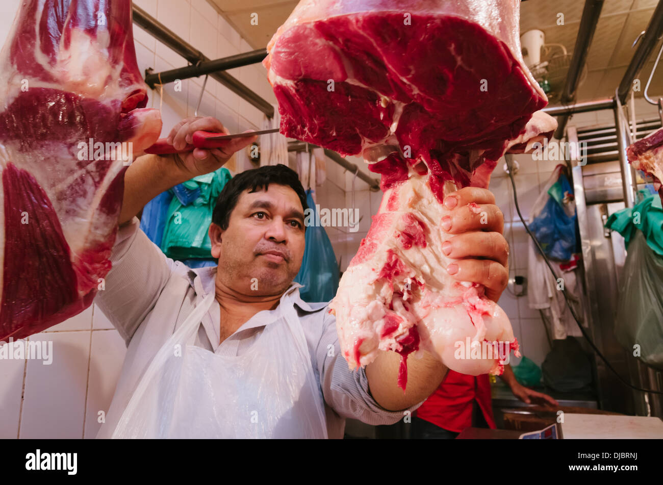 Butcher al lavoro il taglio di carne a fette presso il suo negozio di Deira. Dubai, EAU. Foto Stock