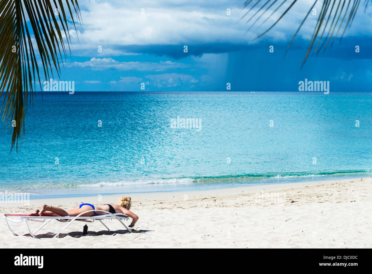 Un giovane biondo donna caucasica sunbathes in una chaise longue a St. Croix, Isole Vergini americane, mentre una tempesta infuria in mare. Foto Stock