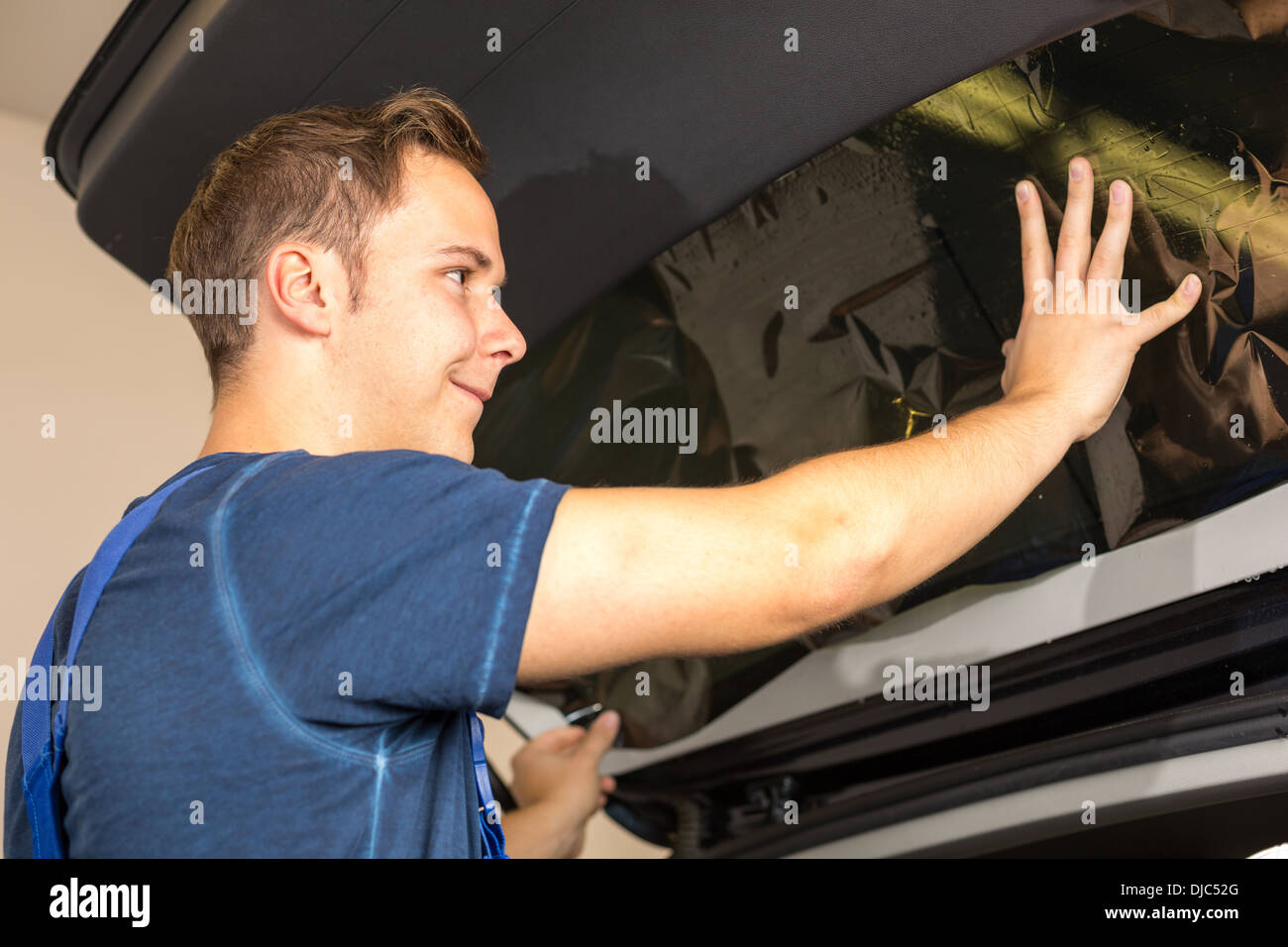 Lavoratore nel garage di colorazione del finestrino di un'automobile con tinte di una lamina o pellicola Foto Stock