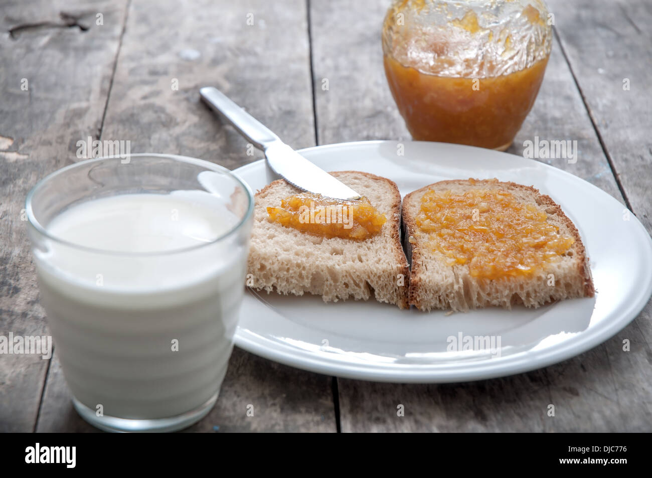 Pane con marmellata di arancia e un bicchiere di latte sul tavolo di legno Foto Stock