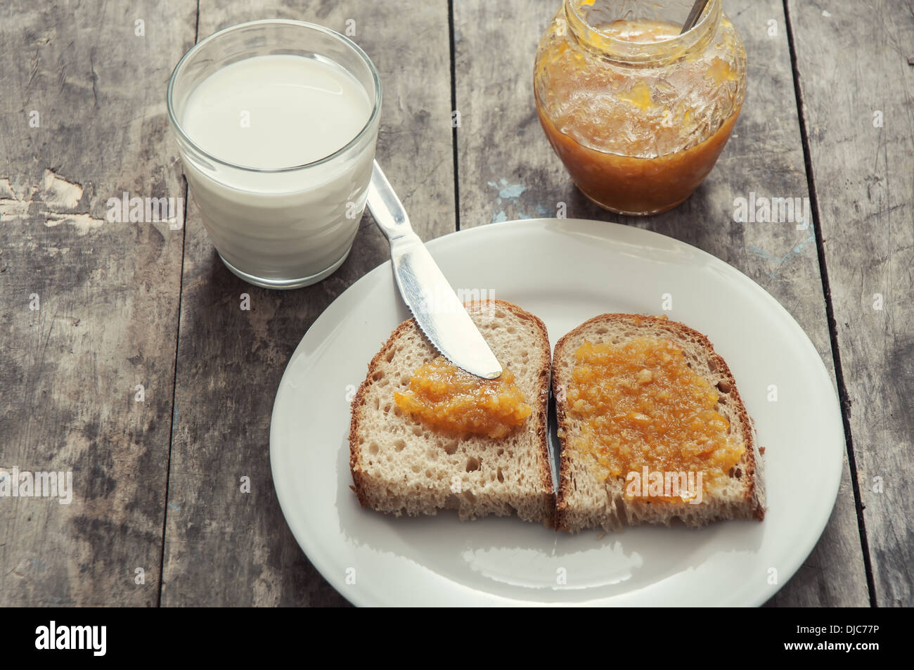 Pane con marmellata di arancia e un bicchiere di latte sul tavolo di legno Foto Stock