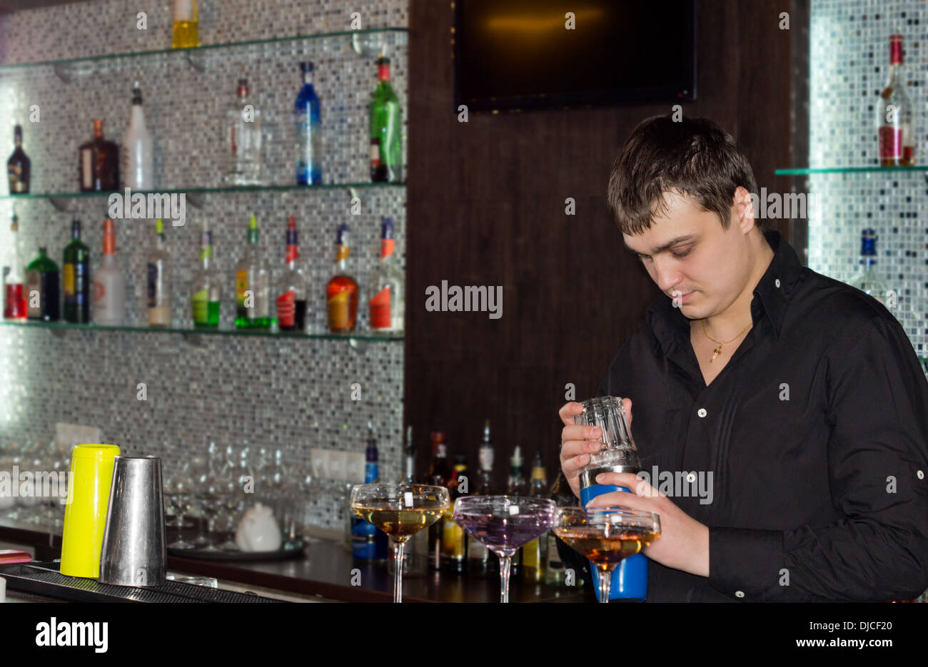 Barman in un pub la preparazione di cocktail alcolico in piedi dietro il bancone la miscelazione di bevande in tre eleganti bicchieri da cocktail Foto Stock