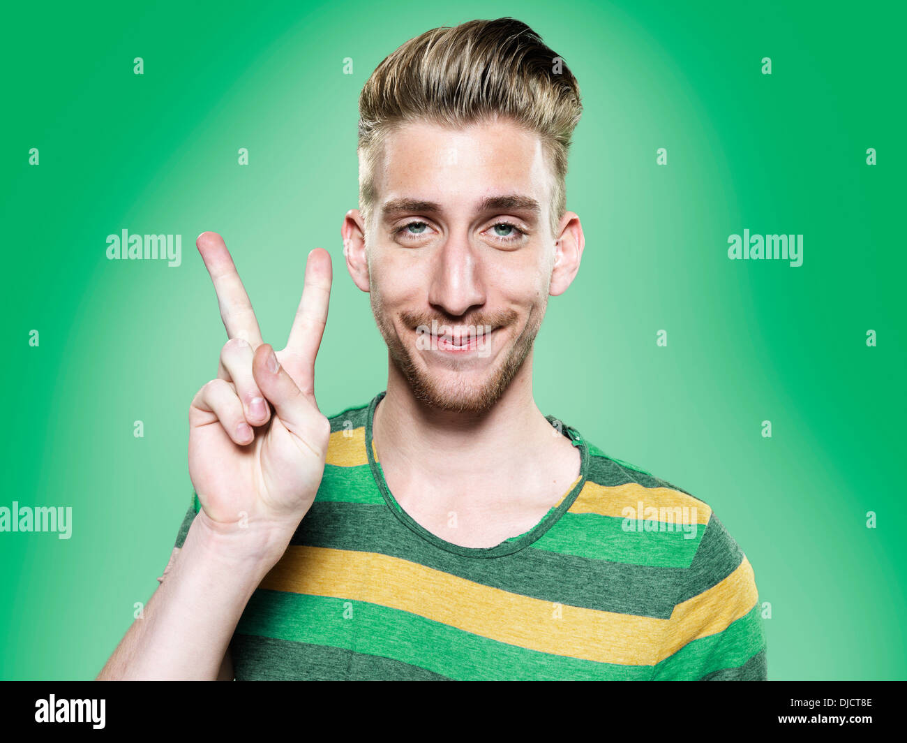 Ritratto di giovane uomo che mostra segno di vittoria, studio shot Foto Stock