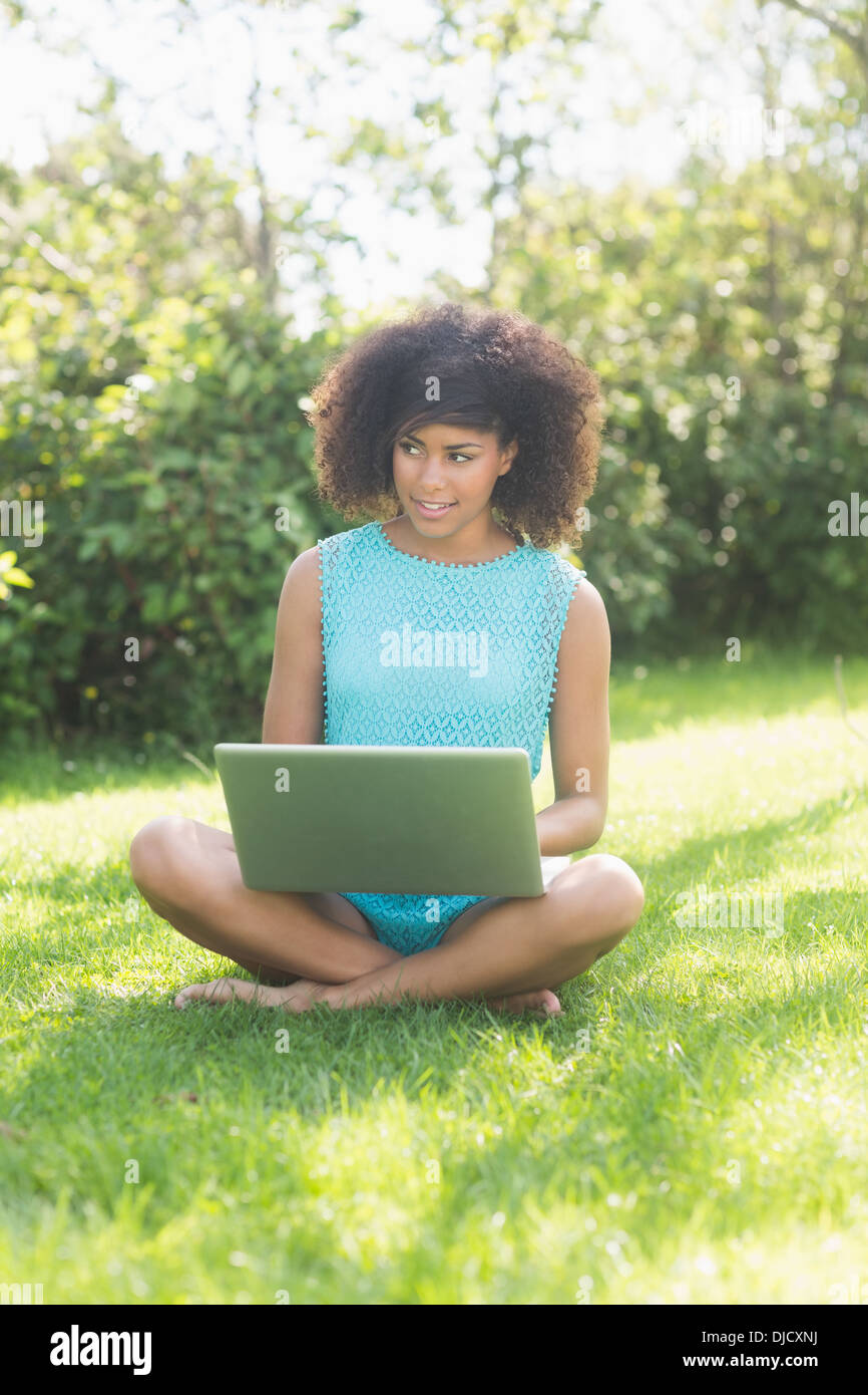 Gorgeous Brunette sorridente seduta zampe trasversale sull'erba utilizzando laptop Foto Stock