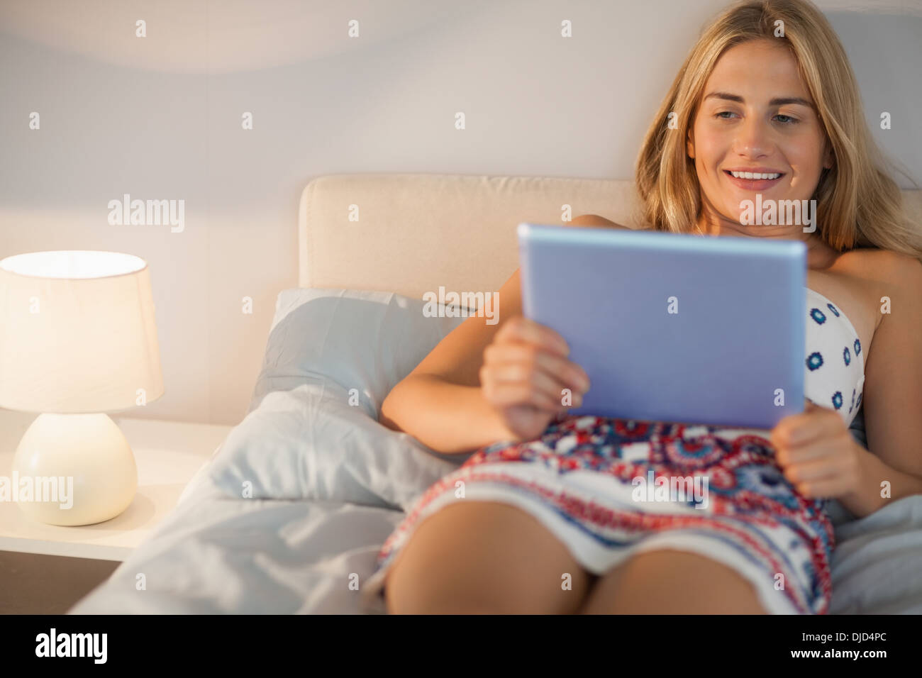 Felice donna che indossa abiti sdraiato sul letto con il suo tablet pc Foto Stock