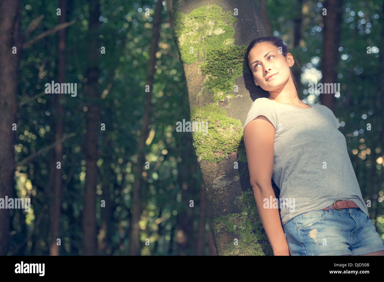 Carino donna informale appoggiato a un albero Foto Stock