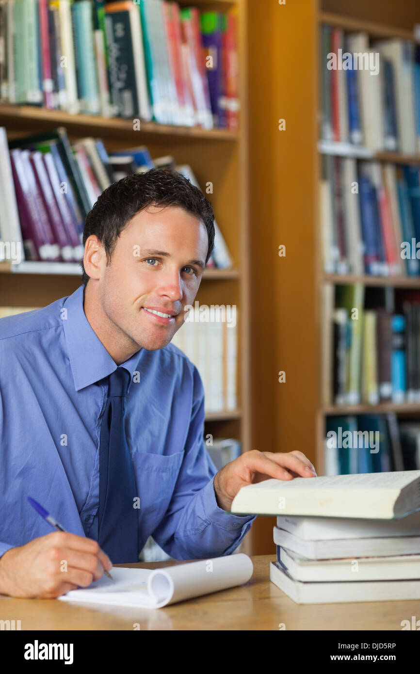 Sorridente bibliotecario seduto alla scrivania prendendo appunti Foto Stock