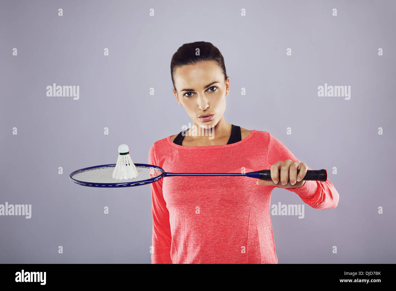 Ritratto di fiducioso giovane ragazza tenendo un badminton racchetta con volano guardando la telecamera contro uno sfondo grigio. Foto Stock