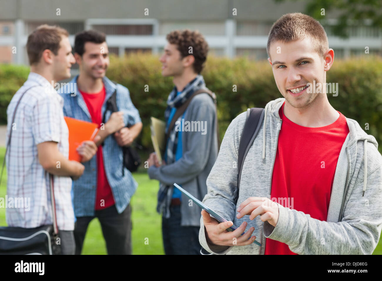 Felice studente maschio utilizzando il suo tablet davanti ai suoi compagni di classe al di fuori Foto Stock