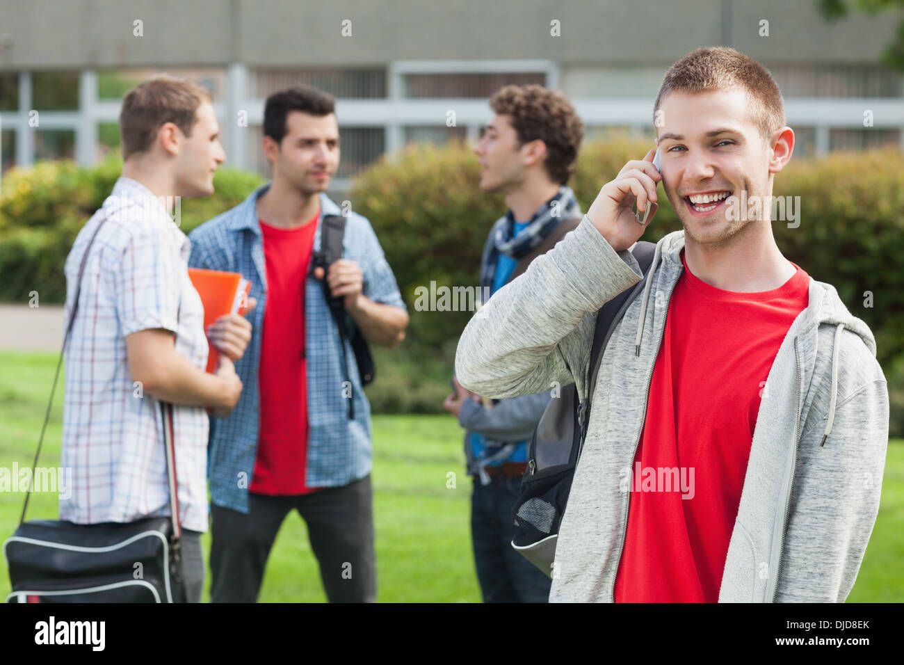 Felice studente maschio sul telefono davanti i suoi compagni di studio al di fuori Foto Stock