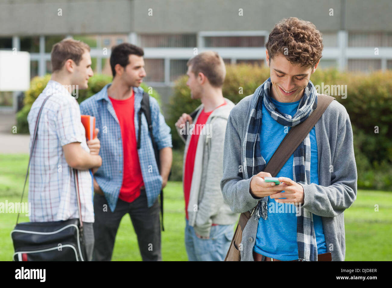 Felice studente maschio inviando un testo davanti ai suoi compagni di classe al di fuori Foto Stock