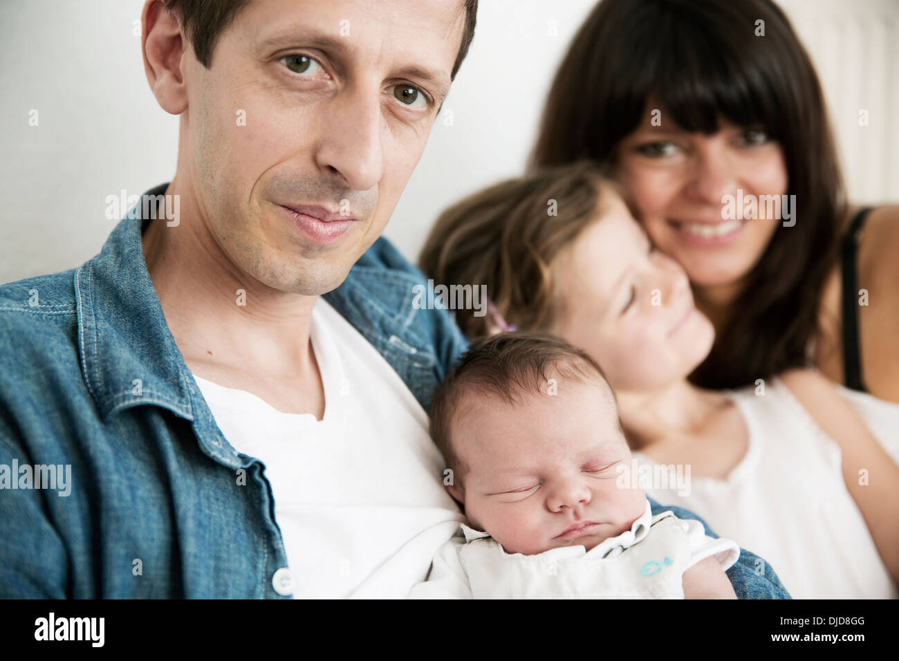 I giovani genitori con neonati maschi e piccola figlia seduti sul divano di casa Foto Stock