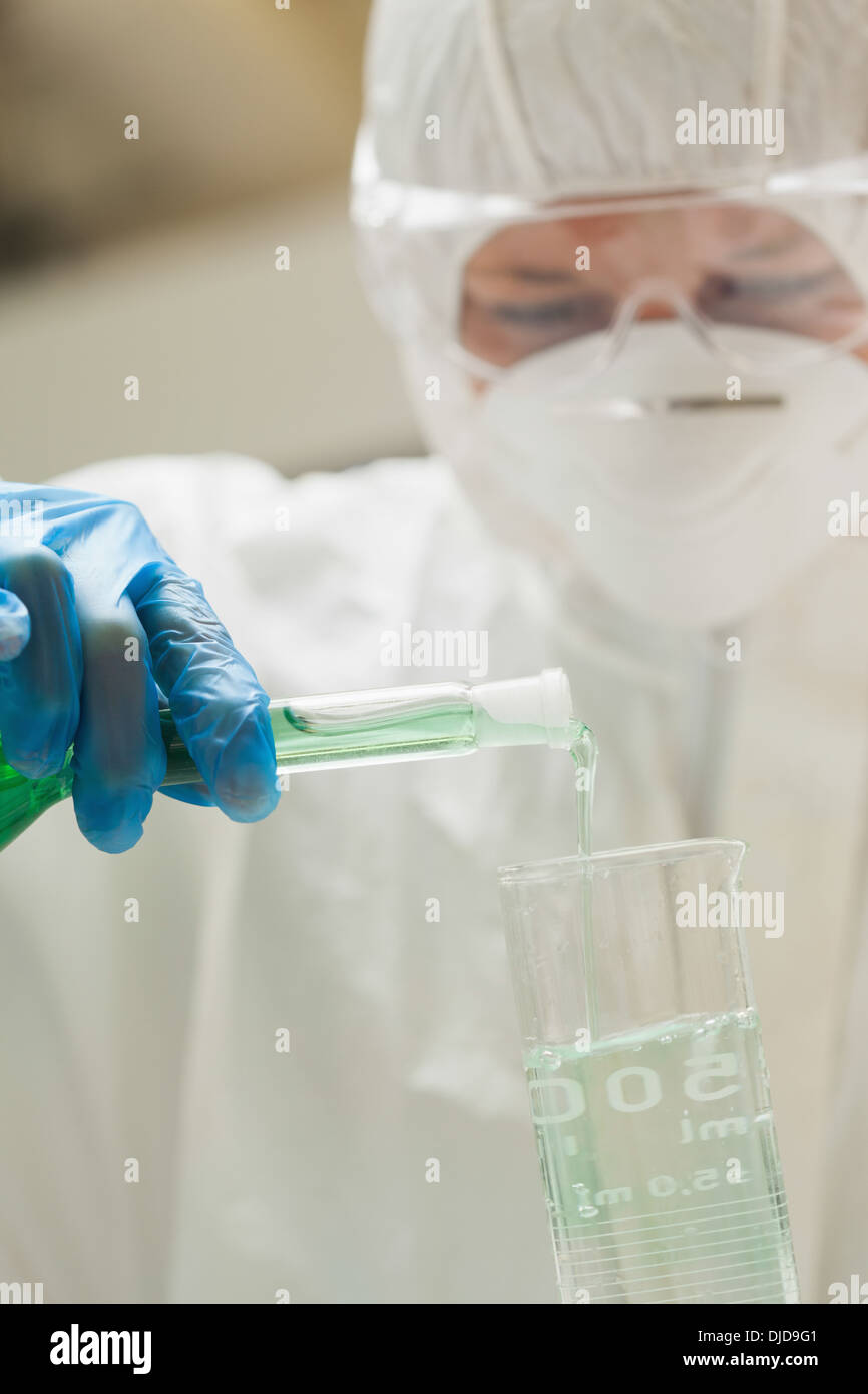 Assistente di laboratorio con maschera versando il liquido nel bicchiere Foto Stock