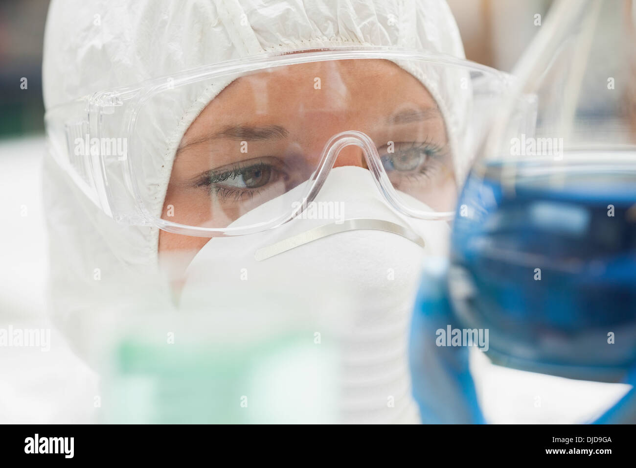 Assistente di laboratorio con maschera guardare vicino a liquido di colore blu Foto Stock