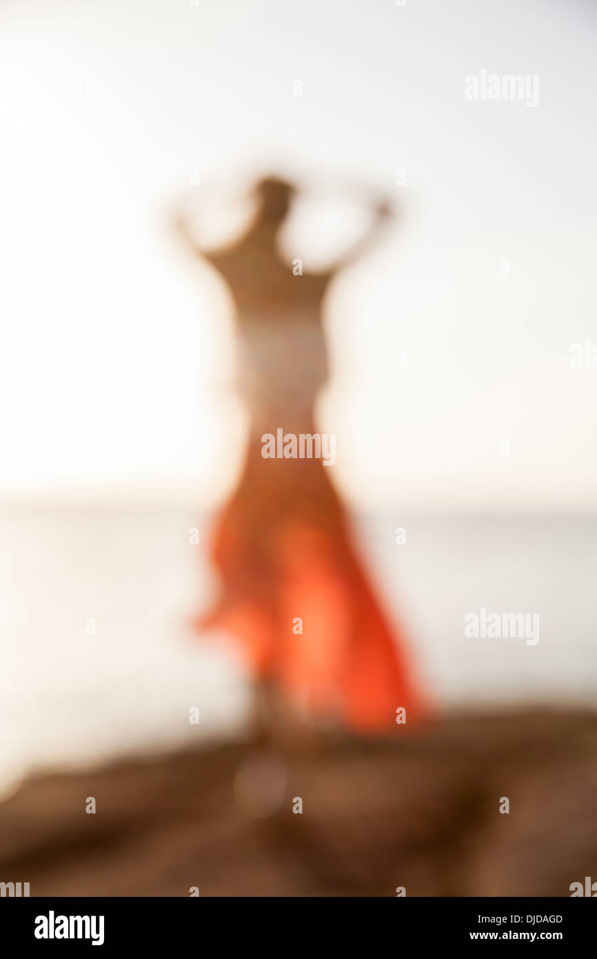 Sfocato fuori fuoco donna nel mantello rosso e bianco superiore camminando sulla scogliera con vista del mare e del cielo in background Foto Stock
