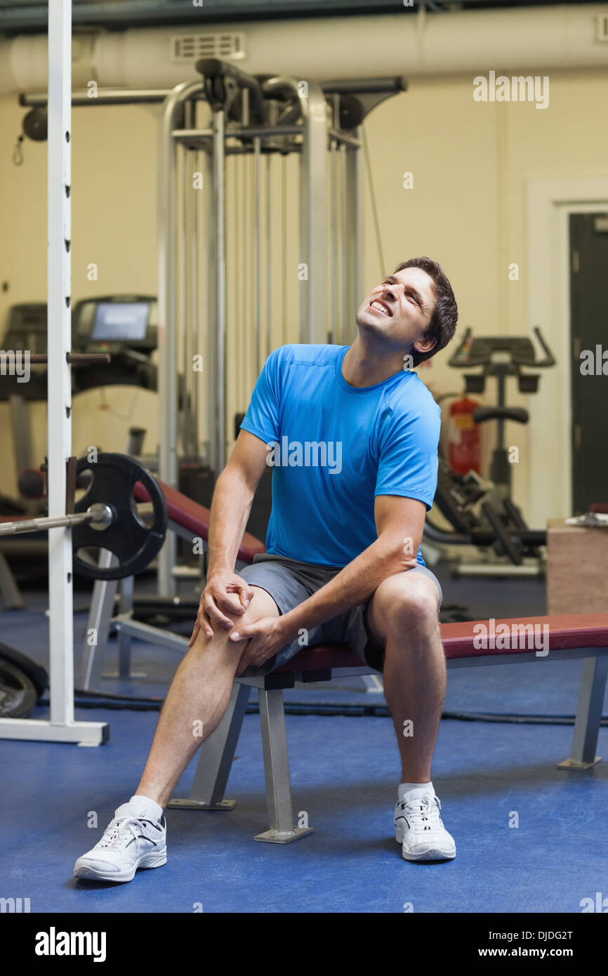 Un sano giovane con un ginocchio infortunato seduto in palestra Foto Stock