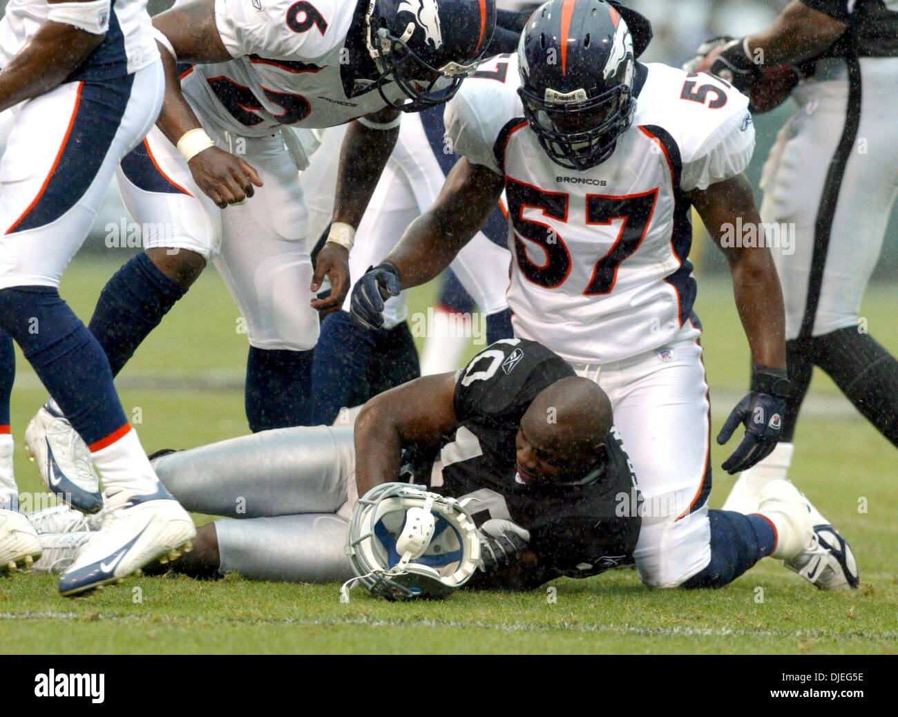 Oct 17, 2004; Oakland, CA, Stati Uniti d'America; NFL Football: con la pioggia è caduta#10 per i raider Carlos Francesco ottiene il suo casco colpisci da #57 per i Broncos Jashon Sykes sul affrontare con #26 per cavalli selvaggii Tatum Bell cerca su nel terzo trimestre. Foto scattata durante i raider vs Broncos gioco presso la Network Associates Coliseum. Foto Stock