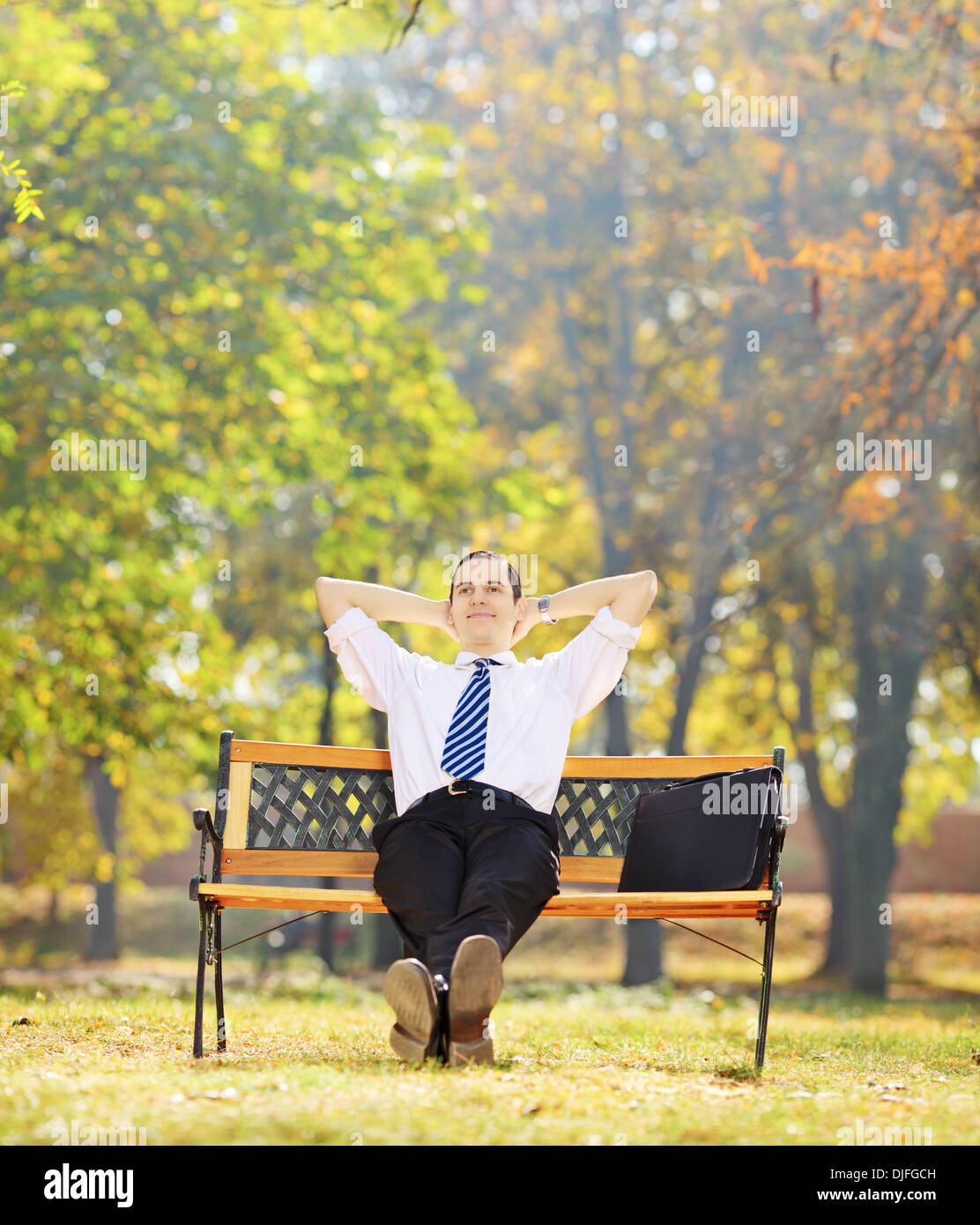 Rilassata imprenditore giovane seduto su una panca di legno in un parco Foto Stock