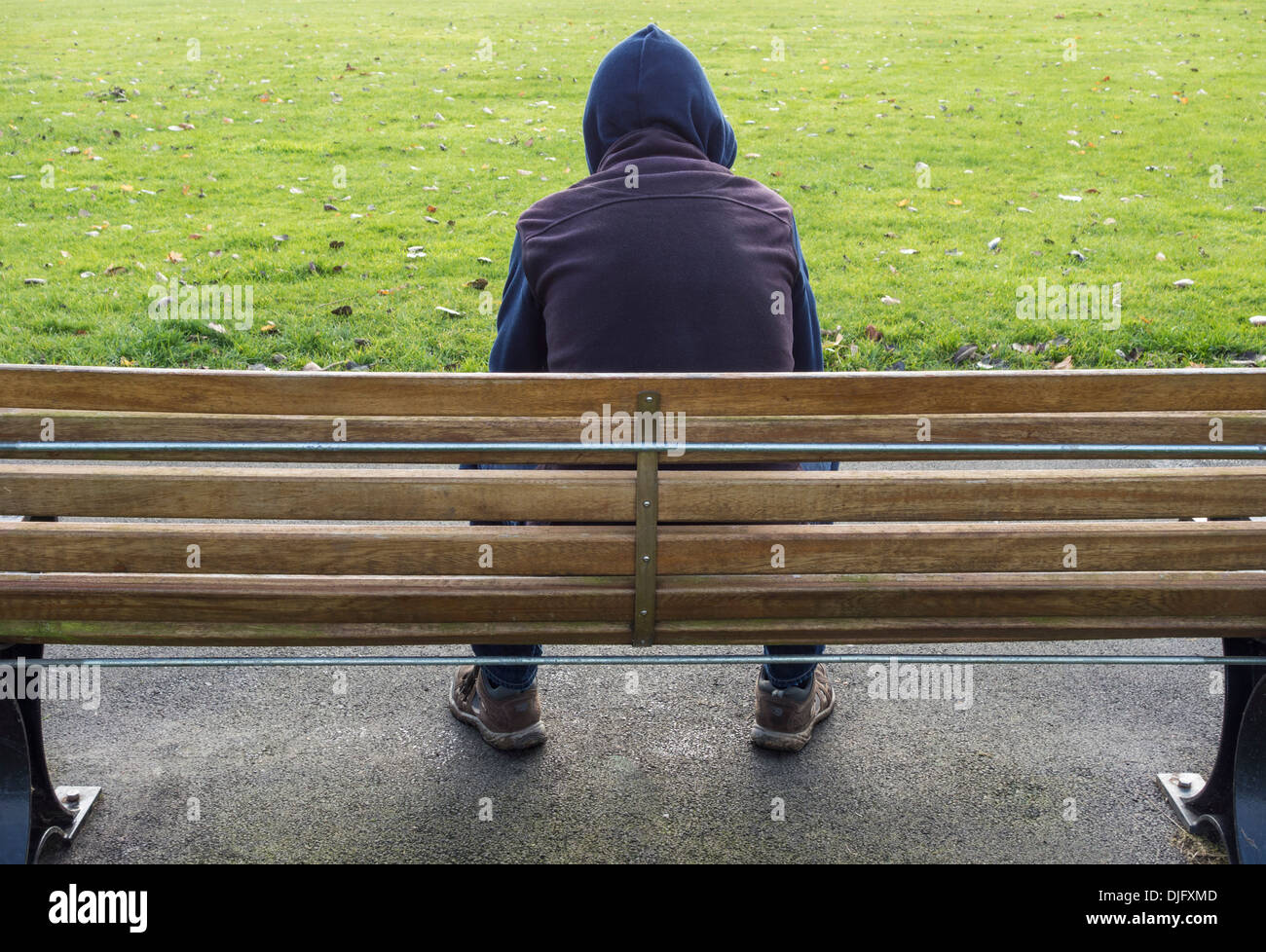 Persona che indossa una felpa con cappuccio seduto sulla panca del parco. salute mentale, solitudine, depressione... Foto Stock