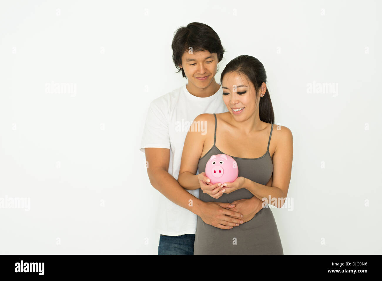 Una giovane coppia asiatica abbraccio, sorridente e tenendo un salvadanaio, il denaro e il concetto di risparmio. Foto Stock