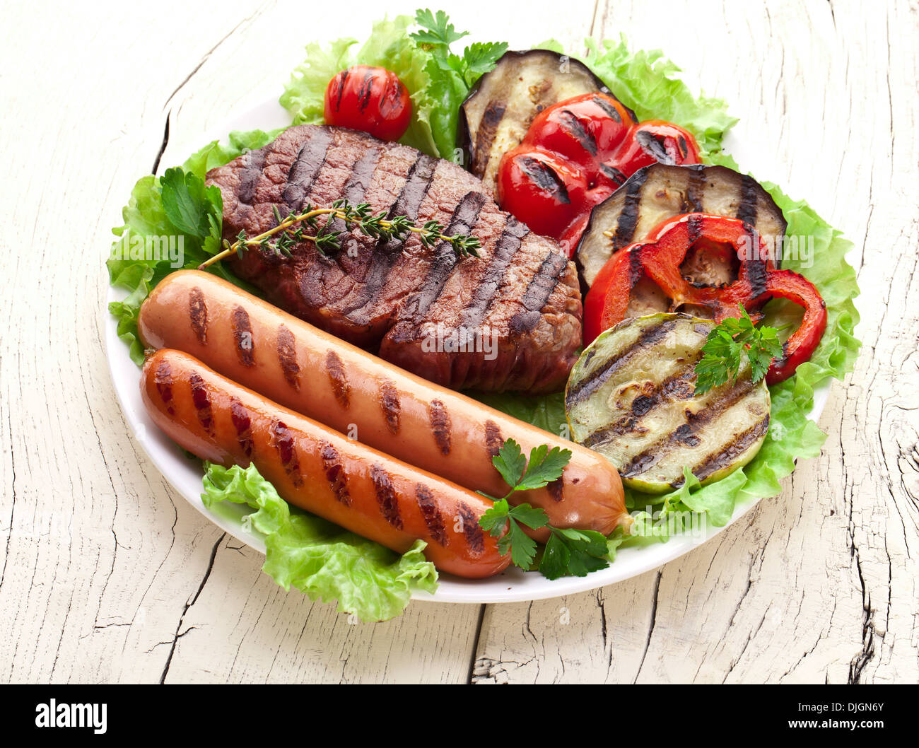 Bistecca alla griglia,salsicce e verdure sopra le foglie di lattuga su un tavolo di legno. Foto Stock