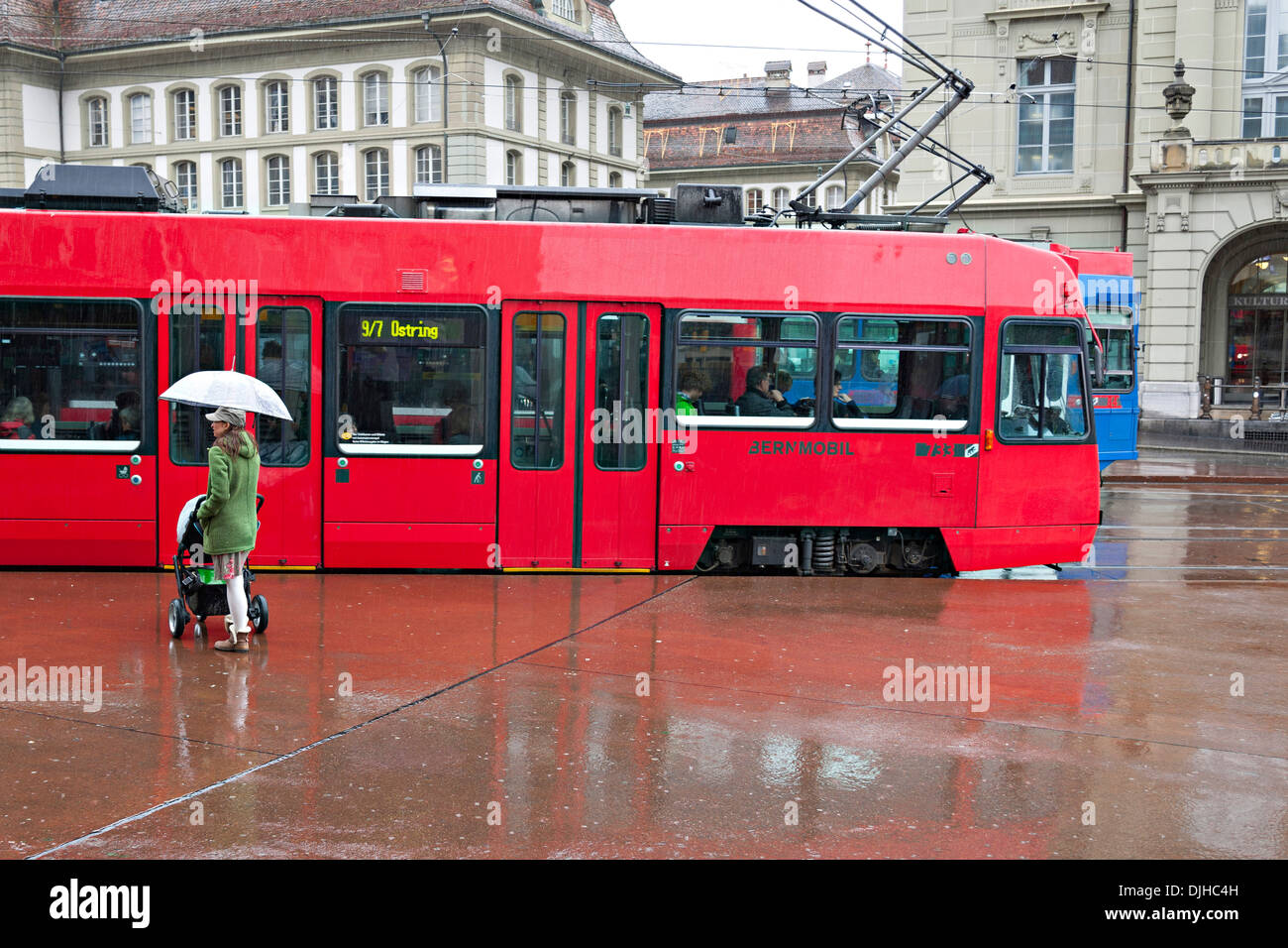 Donna in piedi sotto la pioggia tenendo premuto fino a ombrello rosso con il tram in background, Berna Svizzera Foto Stock