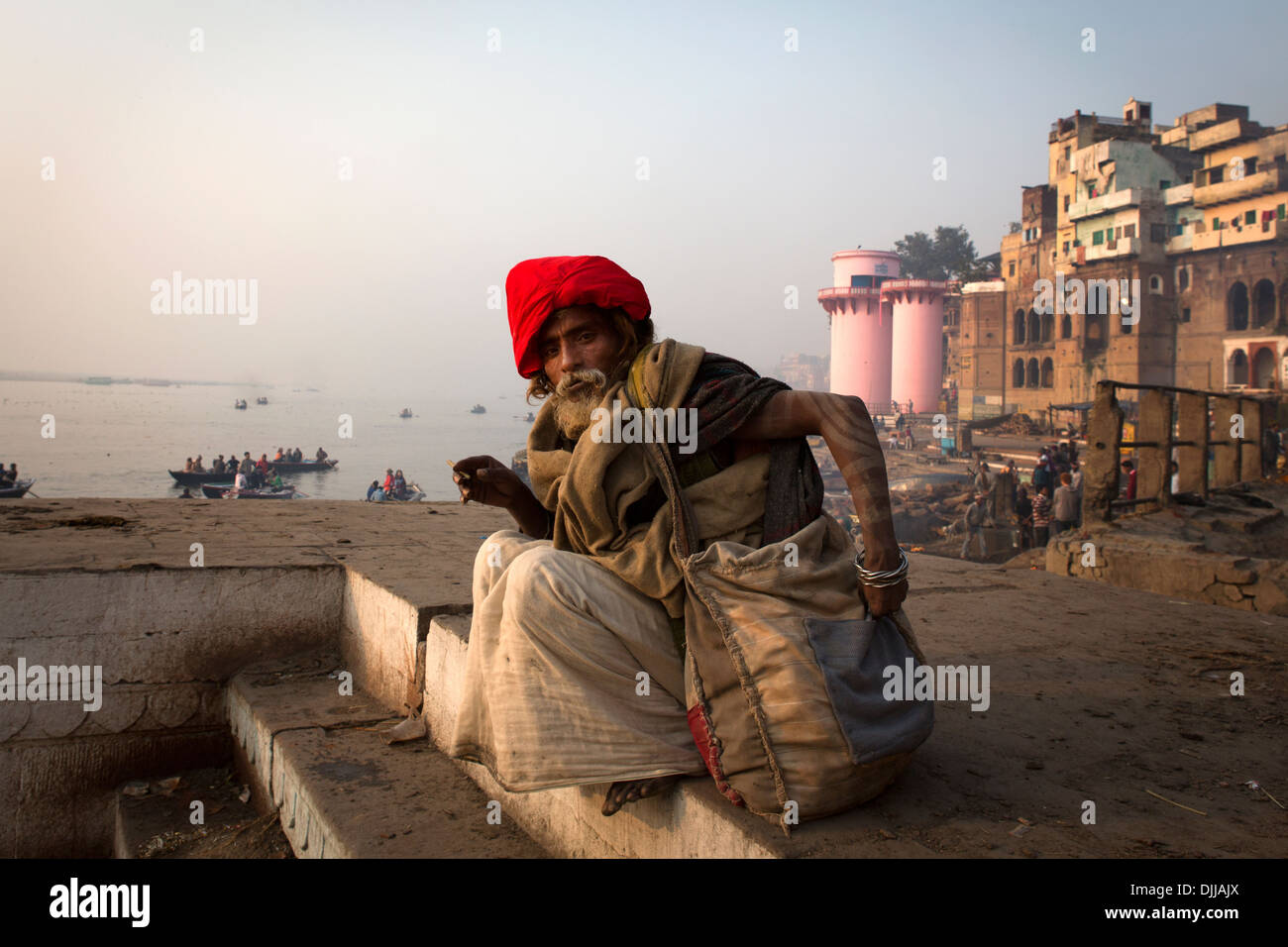 Un pellegrino si siede accanto a Dell il crematorio di Varanasi. Foto Stock