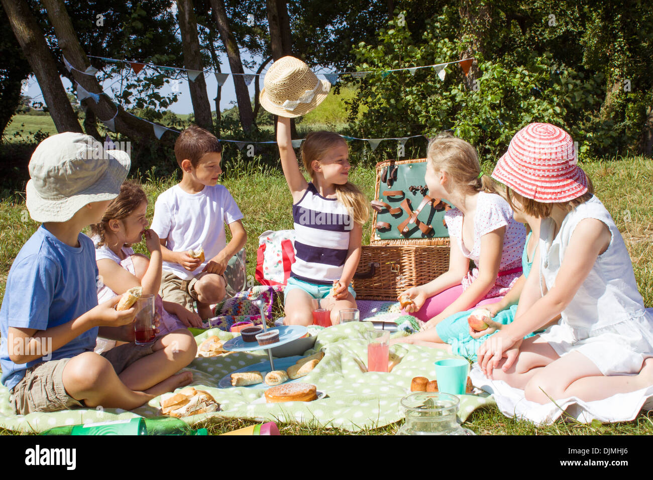 Sette bambini seduti intorno avente un picnic, seduta su una coperta a mangiare cibo nel Somerset, Regno Unito. Foto Stock