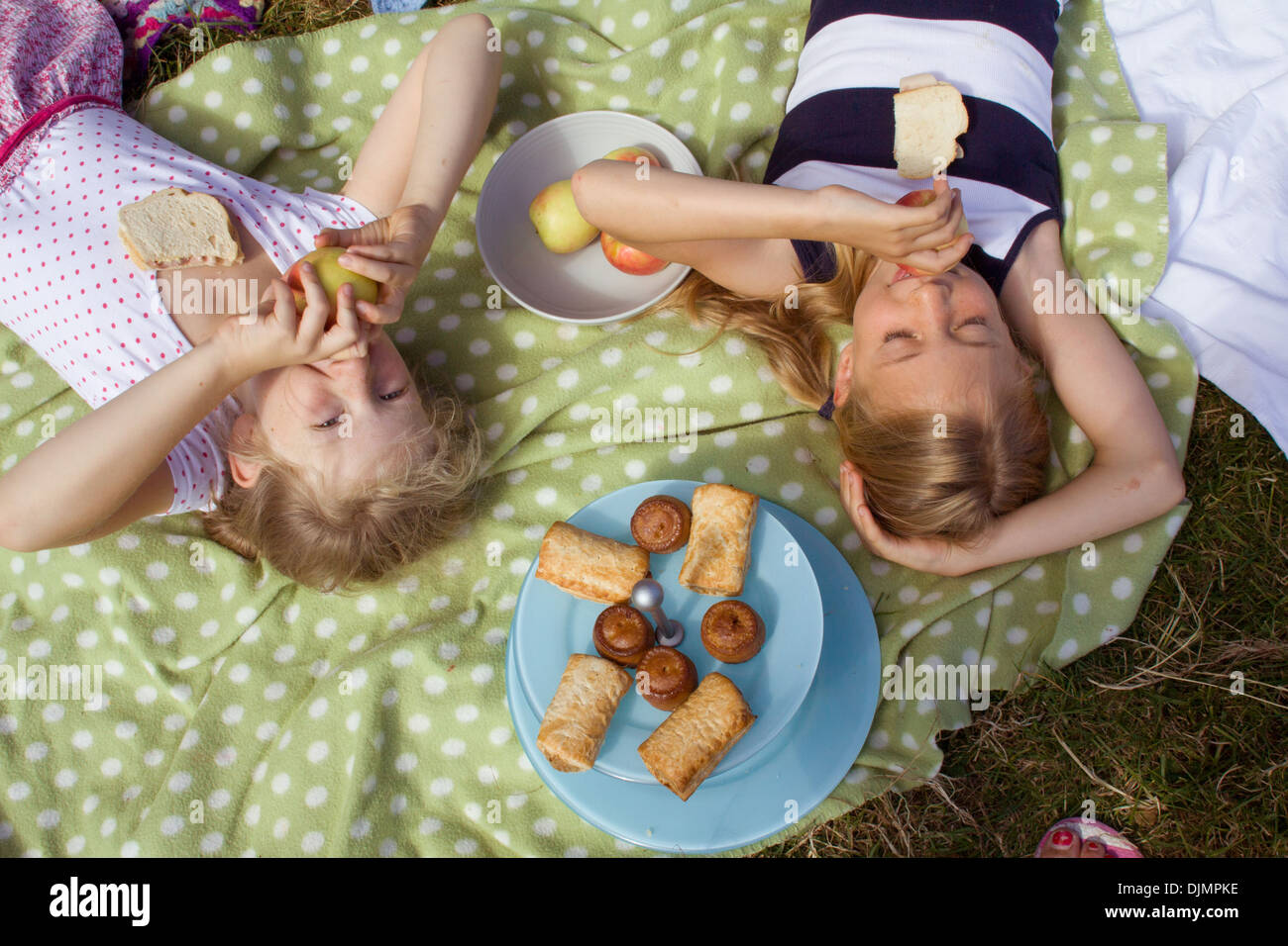 Ragazze sdraiato a mangiare le mele a un picnic, giacente su un macchie coperta di verde nel Somerset, Regno Unito. Foto Stock