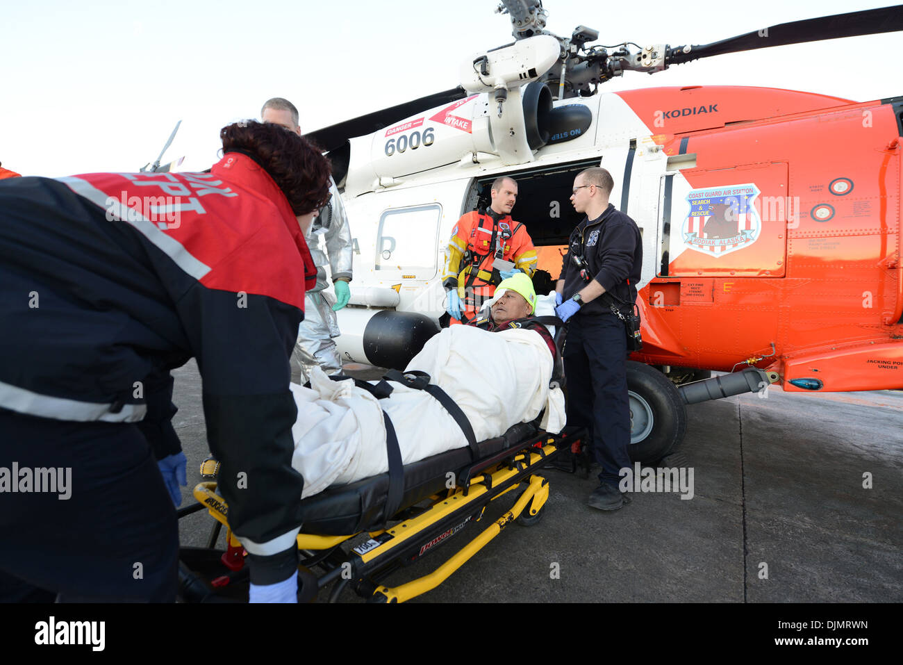 Un Coast Guard MH-60 elicottero Jayhawk equipaggio trasferisce un uomo ferito a un Kodiak City Fire autoambulanza per ulteriore trasferimento al commerciale medevac servizi di Kodiak, Alaska, nov. 27, 2013. L'uomo ferito suo capo e occhio destro durante una caduta a bordo Foto Stock