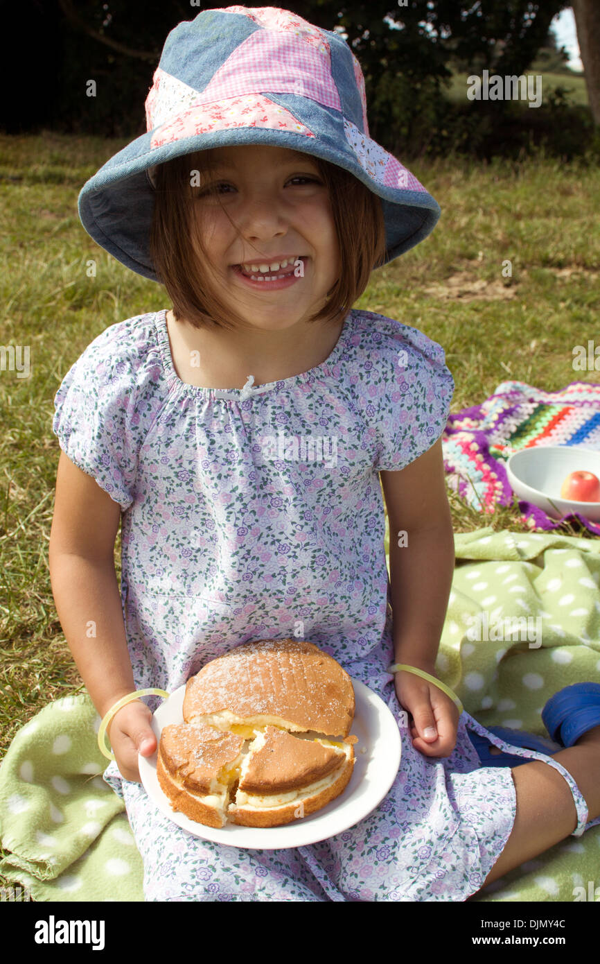 Bambina tenendo la torta su un picnic seduti su una coperta di macchie nel Somerset, Regno Unito. Foto Stock