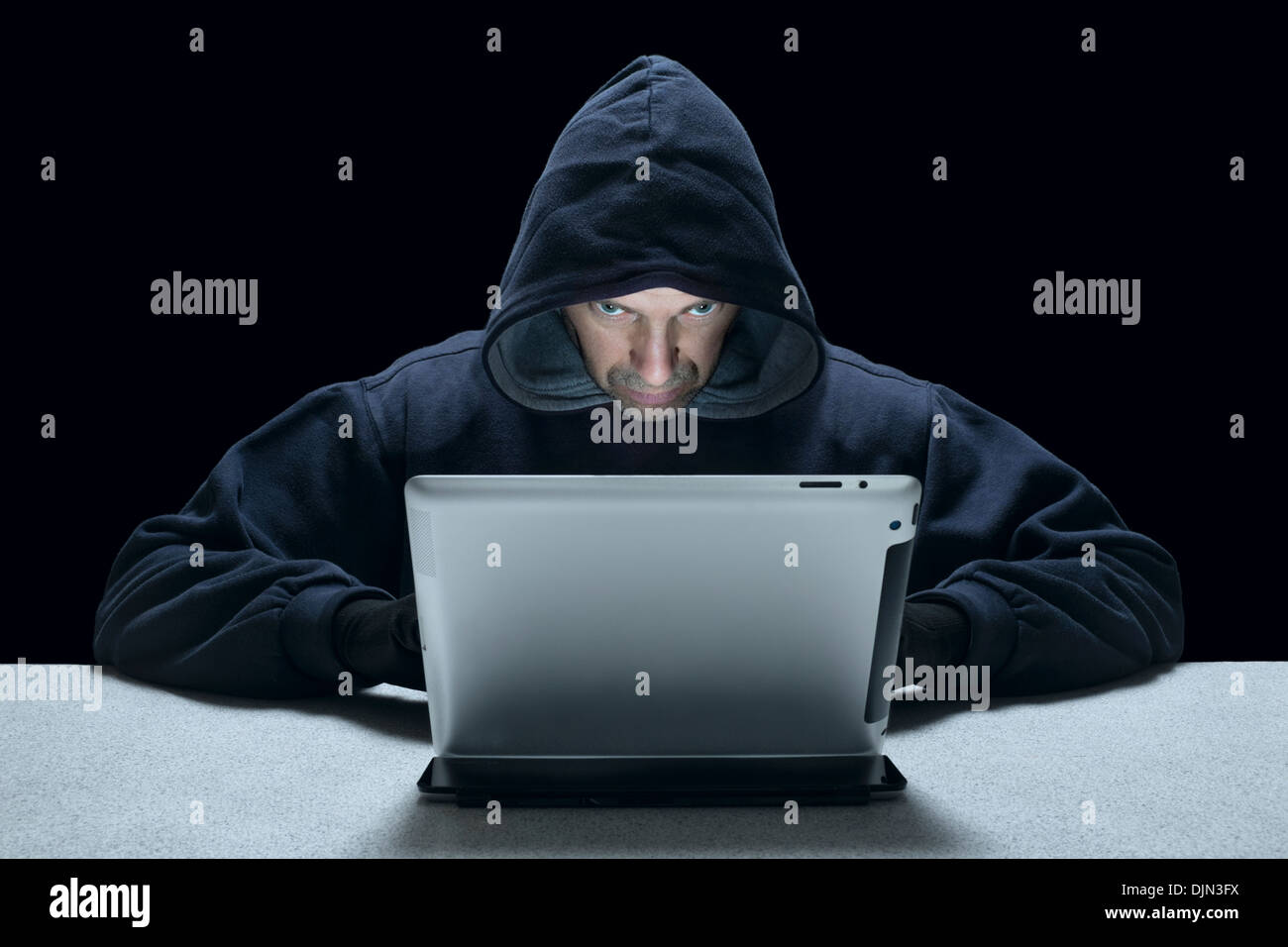 Un uomo incappucciato che rappresenta un cyber criminali, utilizzando un computer tablet. Foto Stock