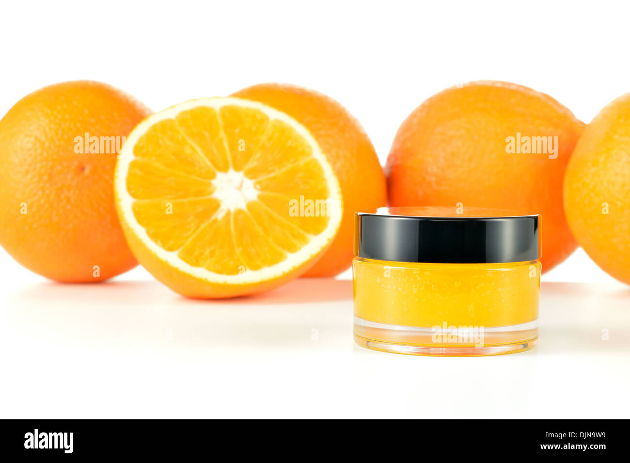 Arancio naturale di zucchero macchia a labbro su sfondo bianco. Cosmetici arancio in un vaso di vetro con le arance in uno sfondo. Foto Stock