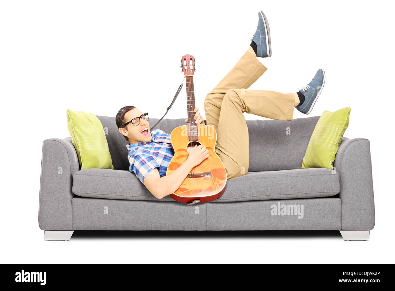 Eccitato giovane maschio sdraiato su un divano moderno e suonando una chitarra acustica Foto Stock