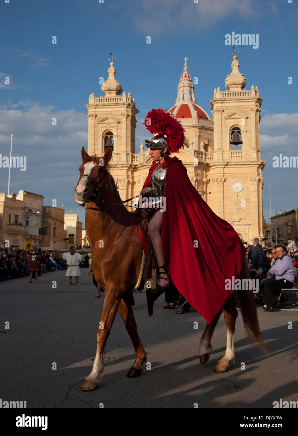 Un uomo vestito come un soldato romano a cavallo sfila per le strade della città durante una rievocazione storica del Venerdì Santo in Malta. Foto Stock