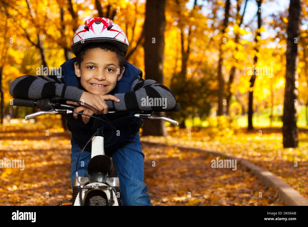 Chiudere ritratto di sorridenti 8 anni black boy in sella a una moto in autunno park appoggiata sulla poppa della bicicletta Foto Stock