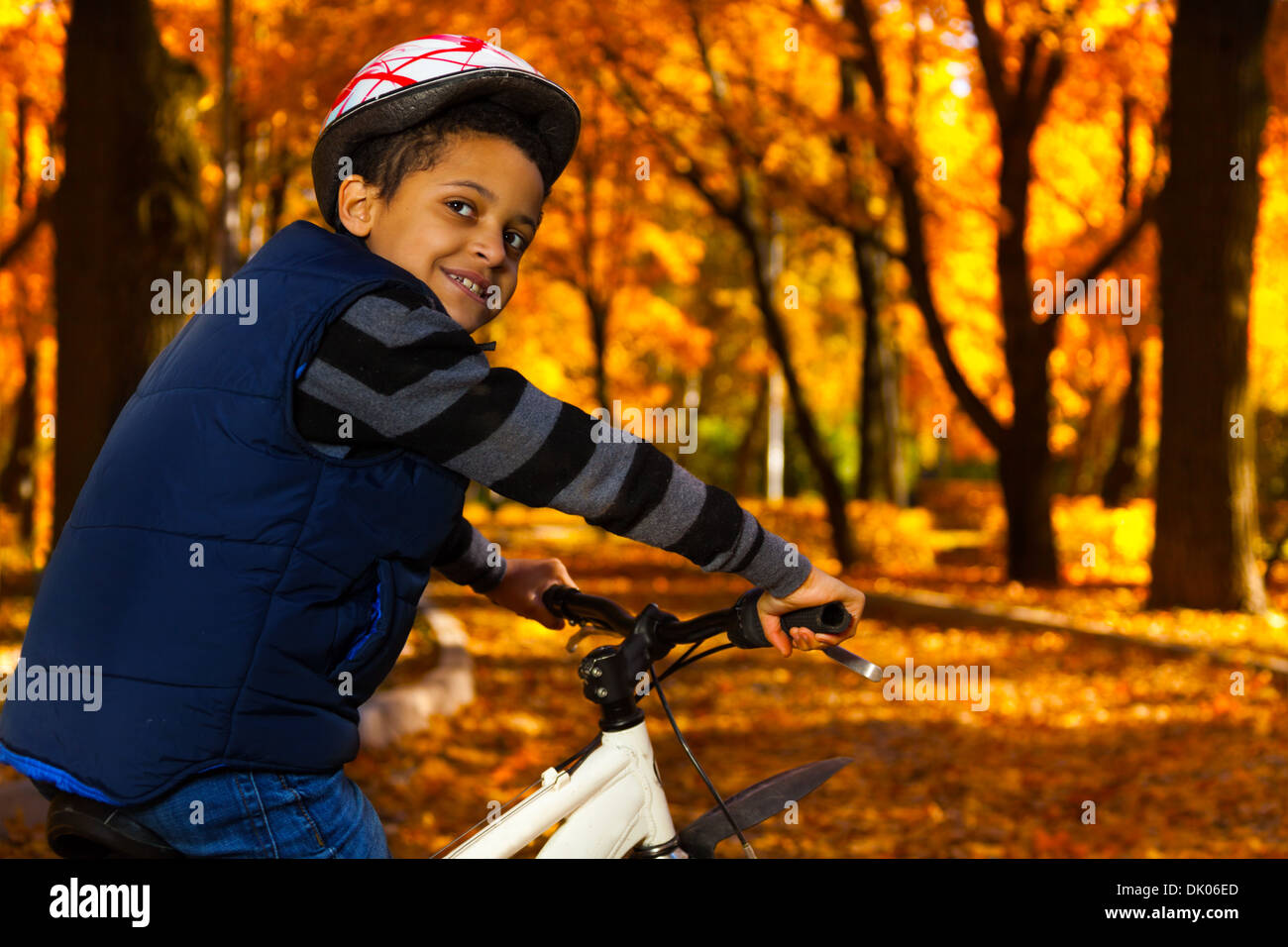 Chiudere ritratto di sorridenti 8 anni black boy in sella a una moto in autunno park appoggiata sulla bicicletta stern rotazione indietro Foto Stock