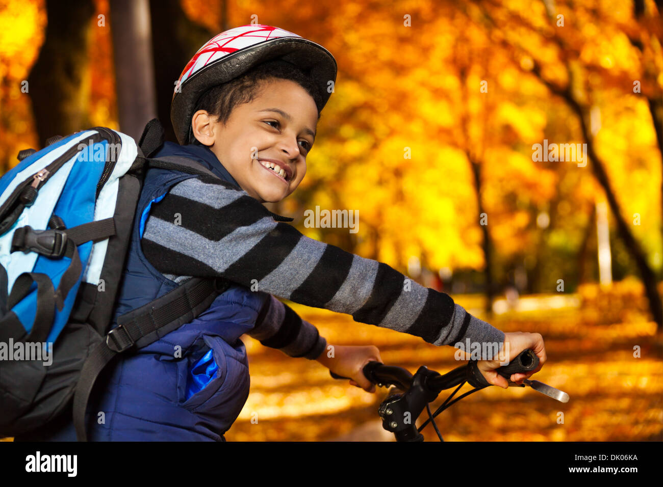 Chiudere ritratto di felice ridere 8 anni black boy con zaino in sella a una moto in autunno park appoggiata sulla bicicletta stern rotazione indietro Foto Stock