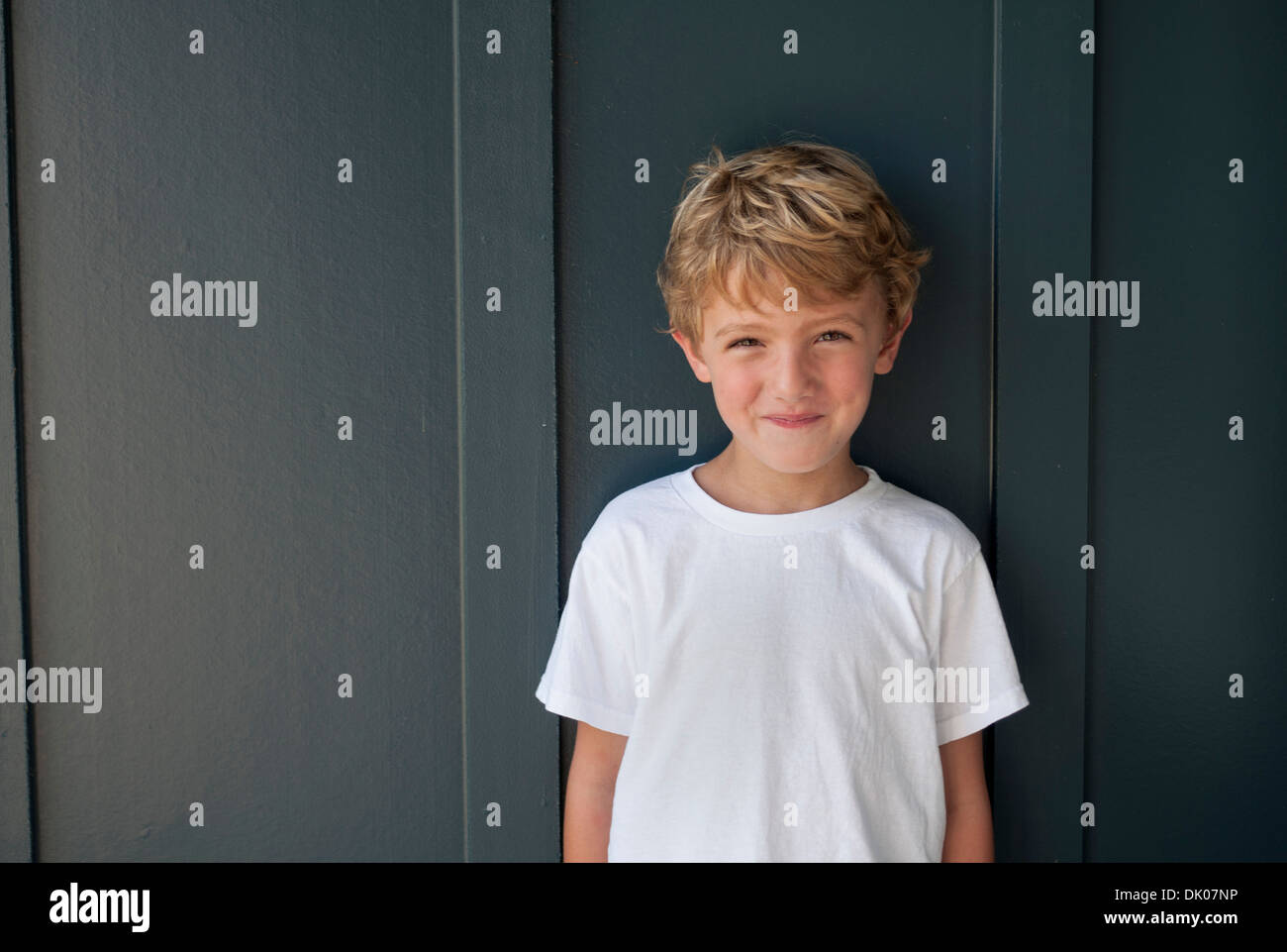 Un signor Caucasian boy, i cinque anni di età, si erge contro una parete di blu. Egli indossa una t-shirt bianco. Foto Stock