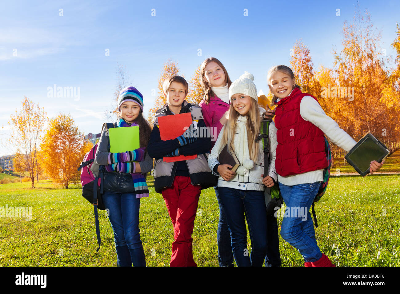 Gruppo di teen i bambini in piedi in autunno parco sulla giornata soleggiata con libri, documenti e gadget Foto Stock