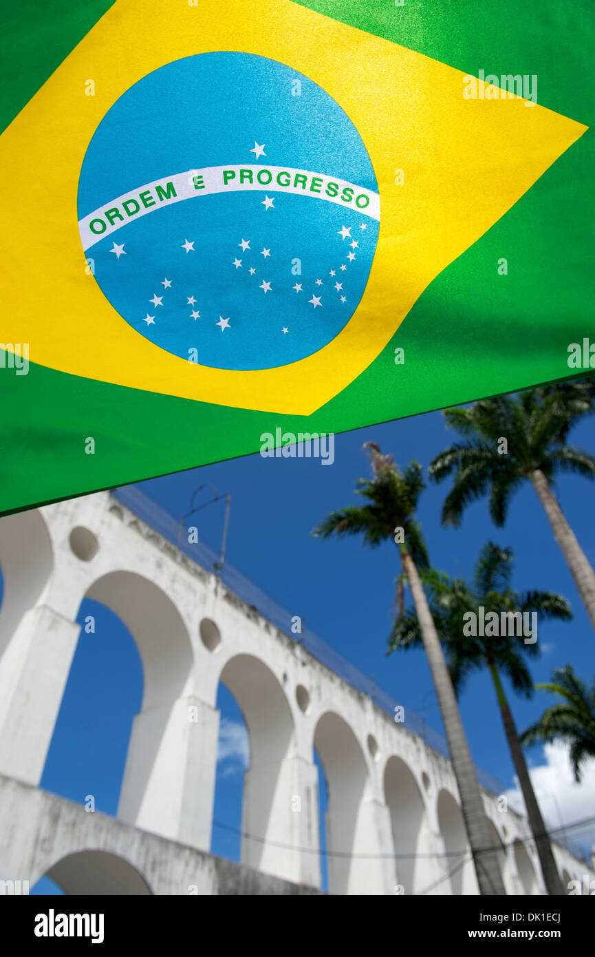 Bandiera brasiliana vola a Lapa archi di Rio de Janeiro in Brasile sotto colori tropicali di cielo blu con palme Foto Stock